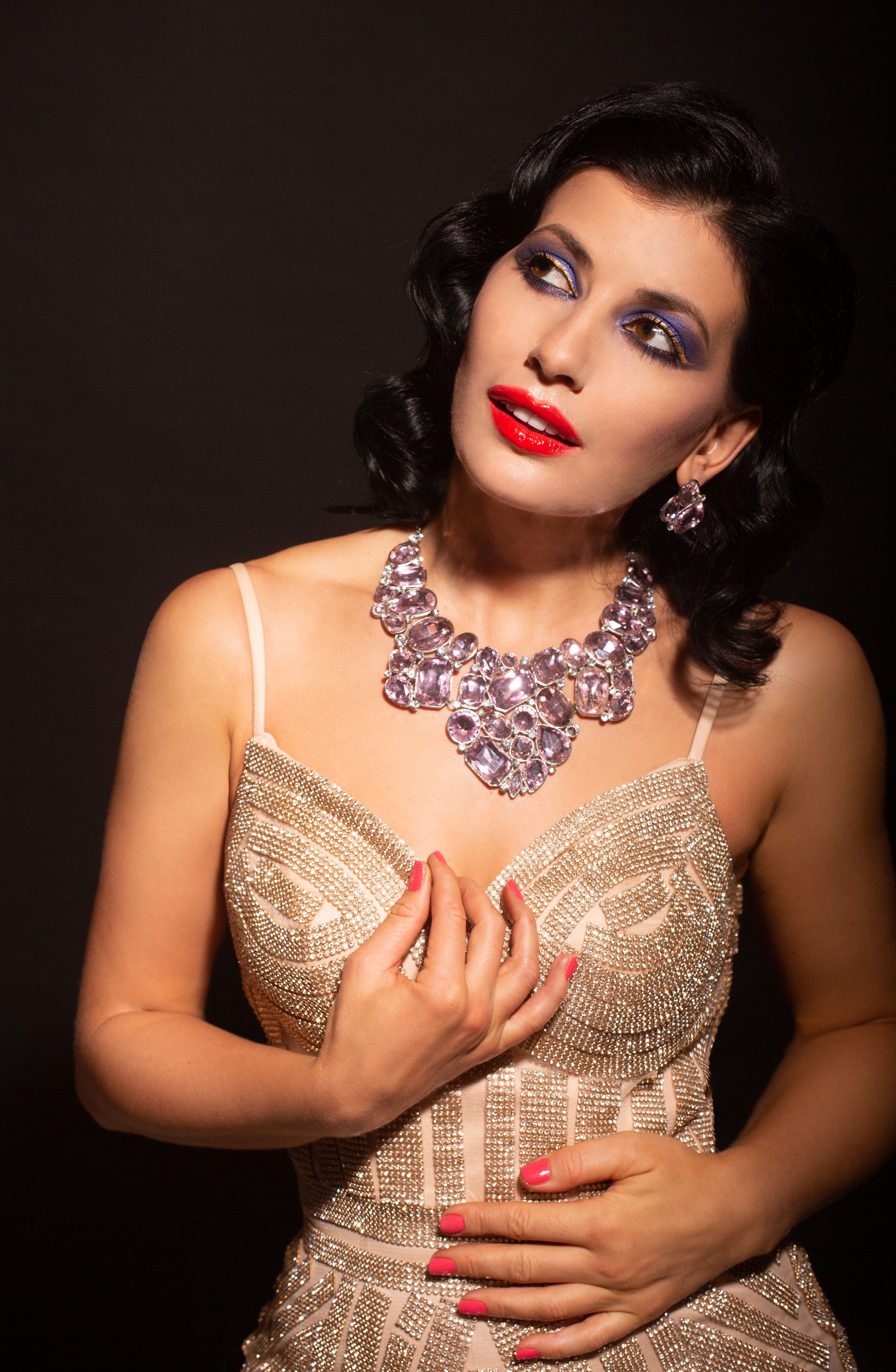 Graceful woman with striking red lips and elegant bead dress posing against a dark background.