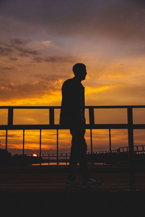 Free A silhouette of a man walking on a bridge at sunset, capturing a tranquil moment in nature. Stock Photo