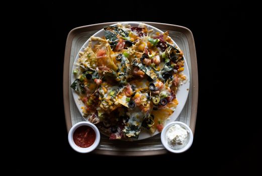 Tasty nachos topped with cheese and olives, served with salsa and sour cream dips.