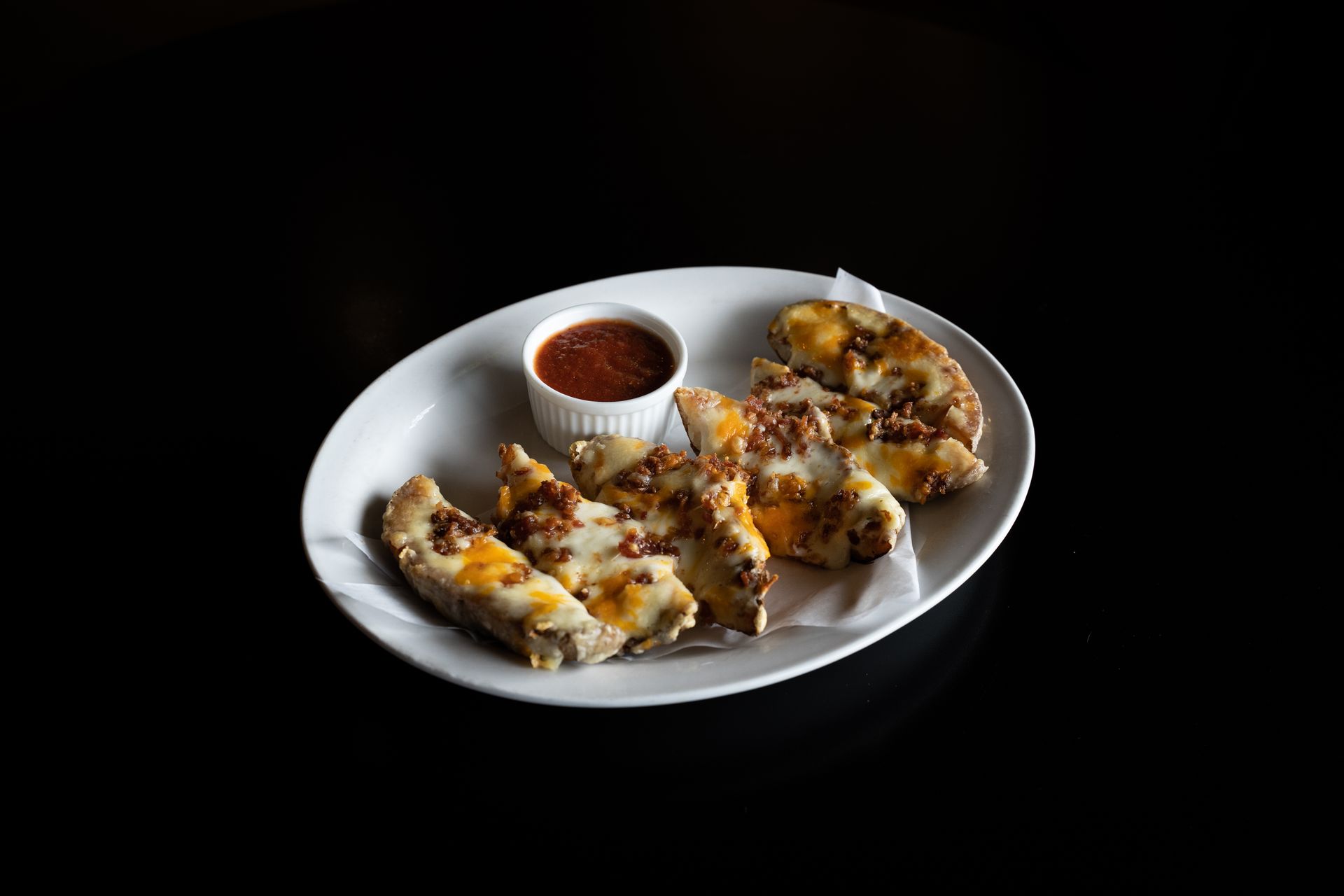 Close-up of cheesy potato wedges with marinara sauce on a white plate.
