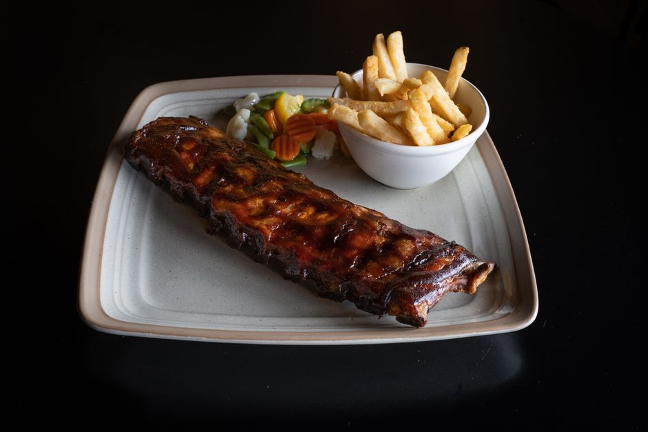A rack of smoked pork spare ribs sliced between the bones, dark bark on the surface and a sticky barbecue glaze pooling on a wooden cutting board.