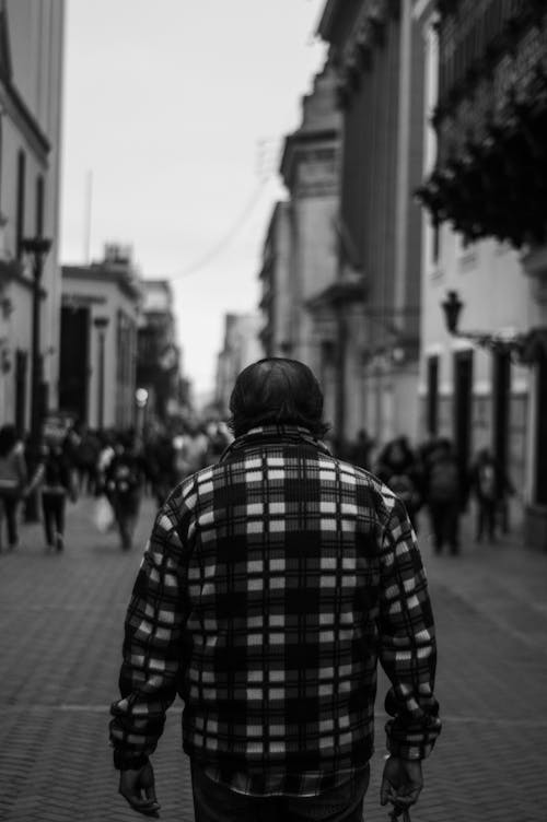Grayscale Photography of Man in Plaid Shirt Walking on Street
