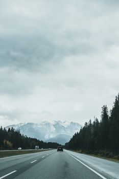 A peaceful highway running through mountainous landscape under a cloudy sky.