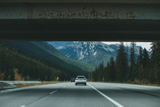 White car driving on a highway underpass with mountain views in the background.