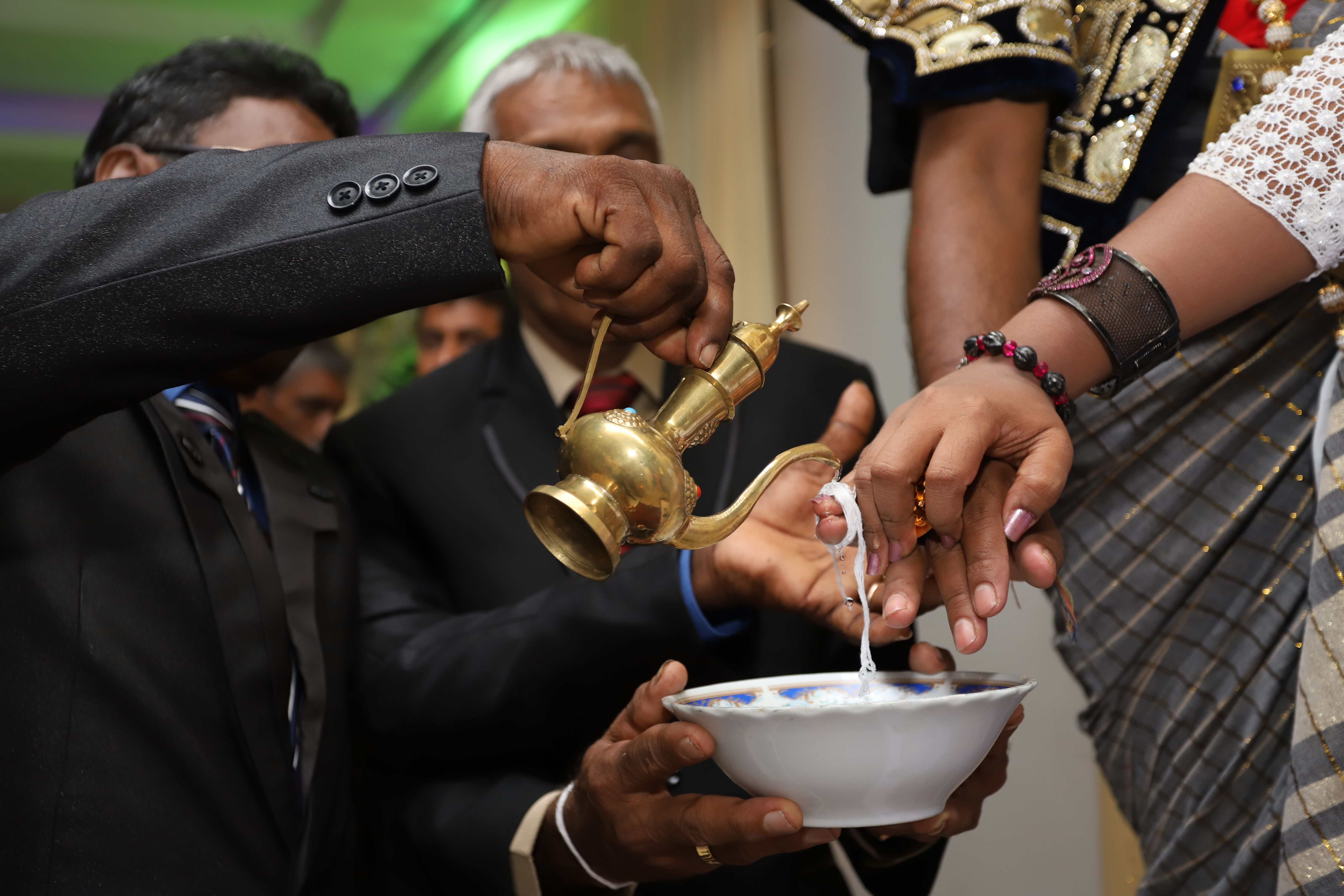 Close-up of hands participating in a traditional Sri Lankan ritual with a golden vessel pouring.