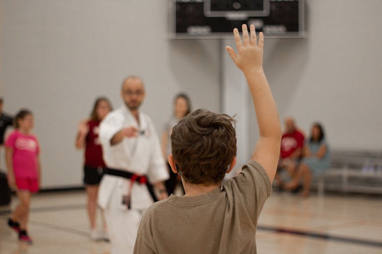 A Boy In Brown Shirt Raising His Hand