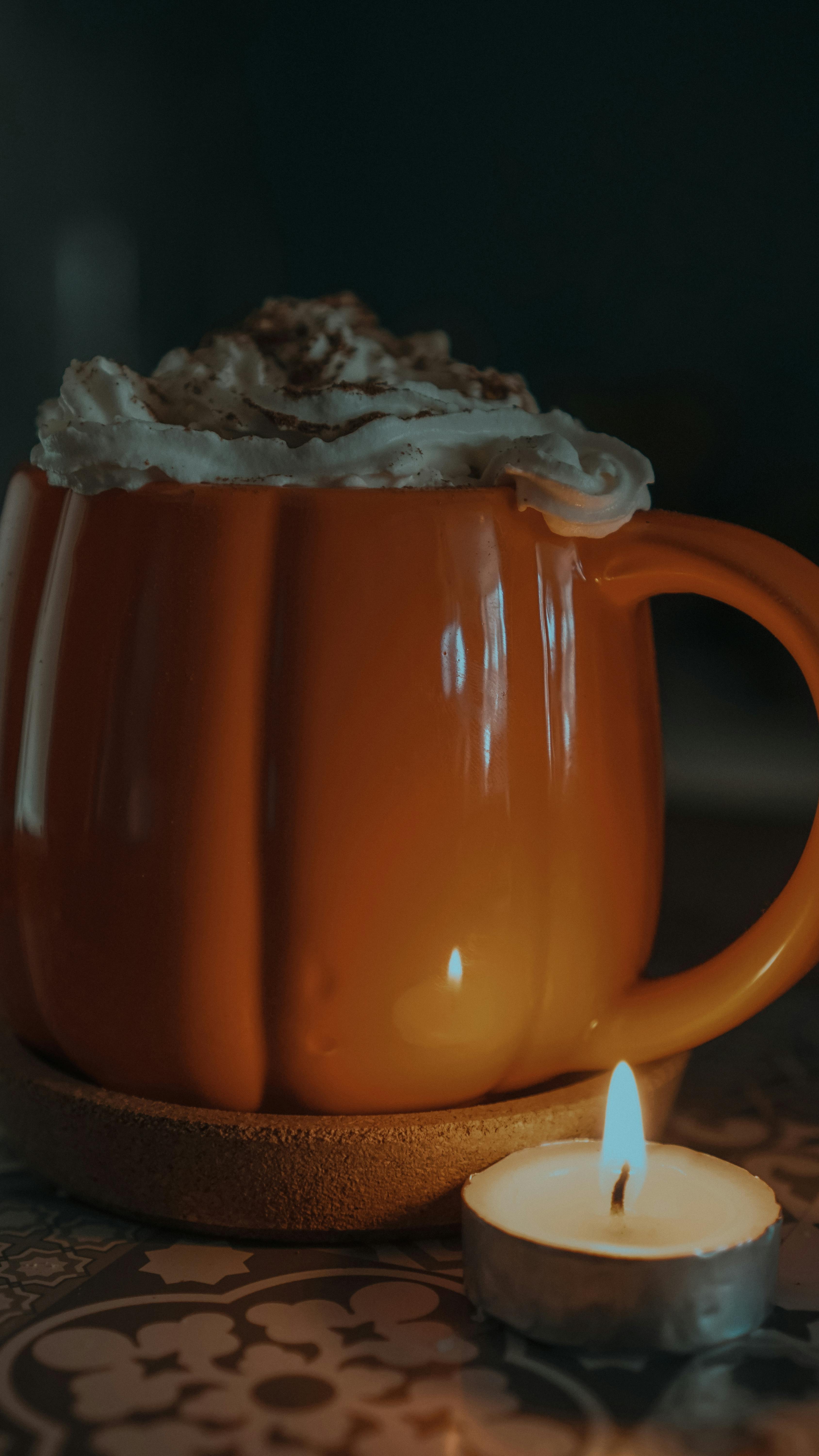 Warm autumn drink in a pumpkin-shaped mug with whipped cream and candlelight.