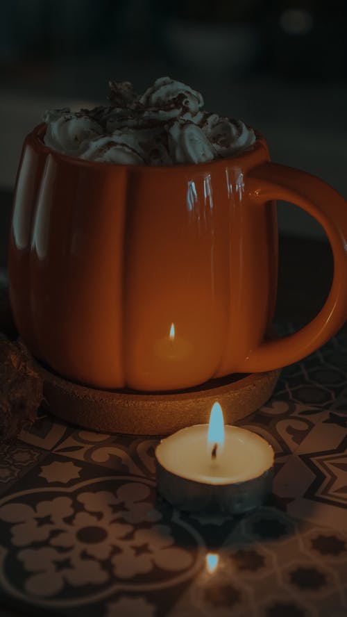 Free Hot Drink on Orange Ceramic Mug Near Lighted Candle Stock Photo