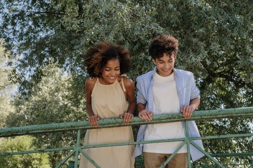 Free Smiling young couple standing together by a metal railing in a lush green park. Stock Photo
