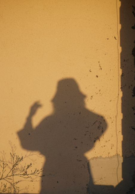 A silhouette of a person with a hat gesturing on a textured yellow wall during sunset.