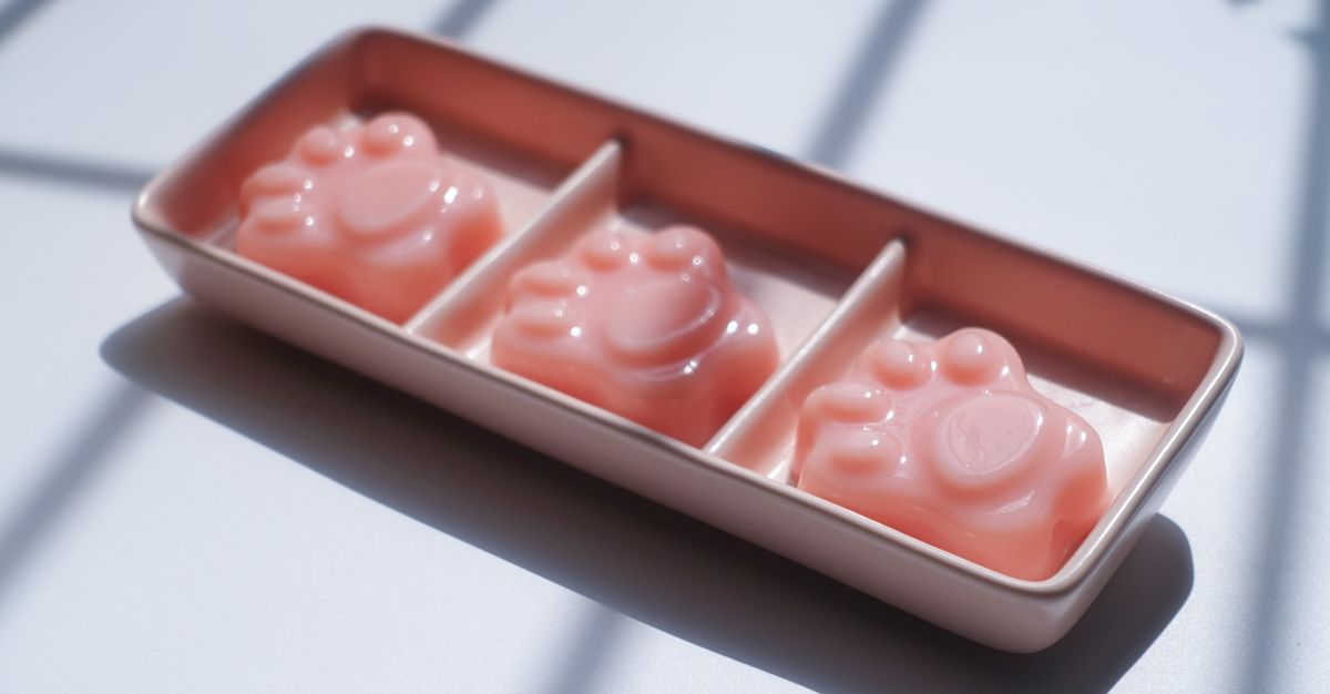 Close-up of pastel pink paw-shaped jelly candies in a decorative tray on a sunny day.