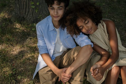 A young couple enjoys a peaceful moment outdoors under the shade of a tree.