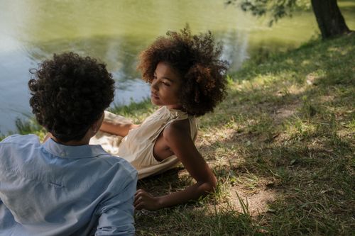 Free Teenage couple enjoying a serene moment together by the lakeside on a sunny day. Stock Photo
