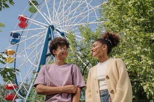 Teenagers standing under ferris wheel and looking at each other with smile