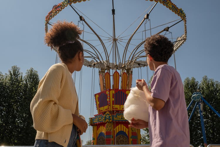 Teenage Couple On Date In Amusement Park Looking At Big Carousel