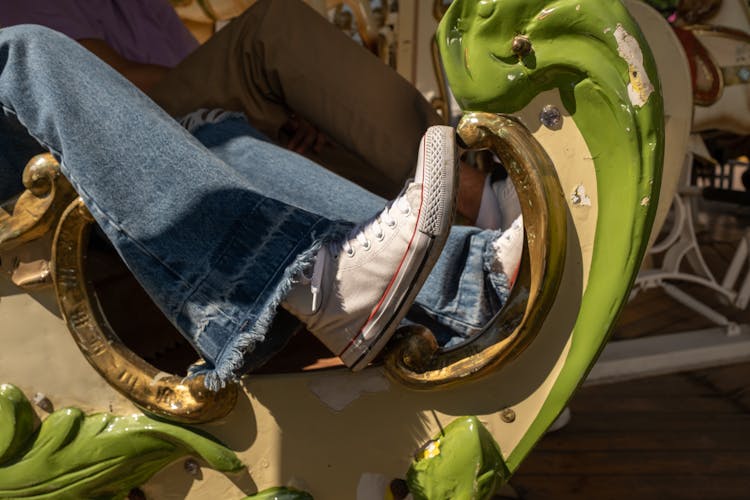 Legs In Blue Jeans And Converse All Star Hiding In Carousel Imitation Of Sledges