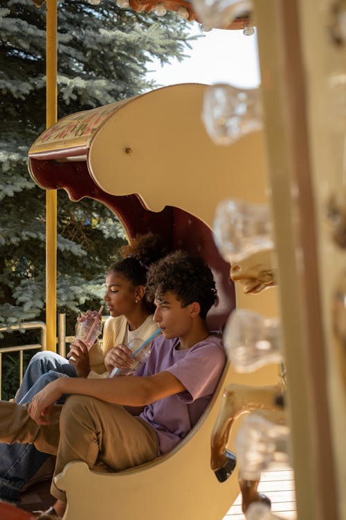 Teenage couple sitting in carousel seat and drinking cold drinks