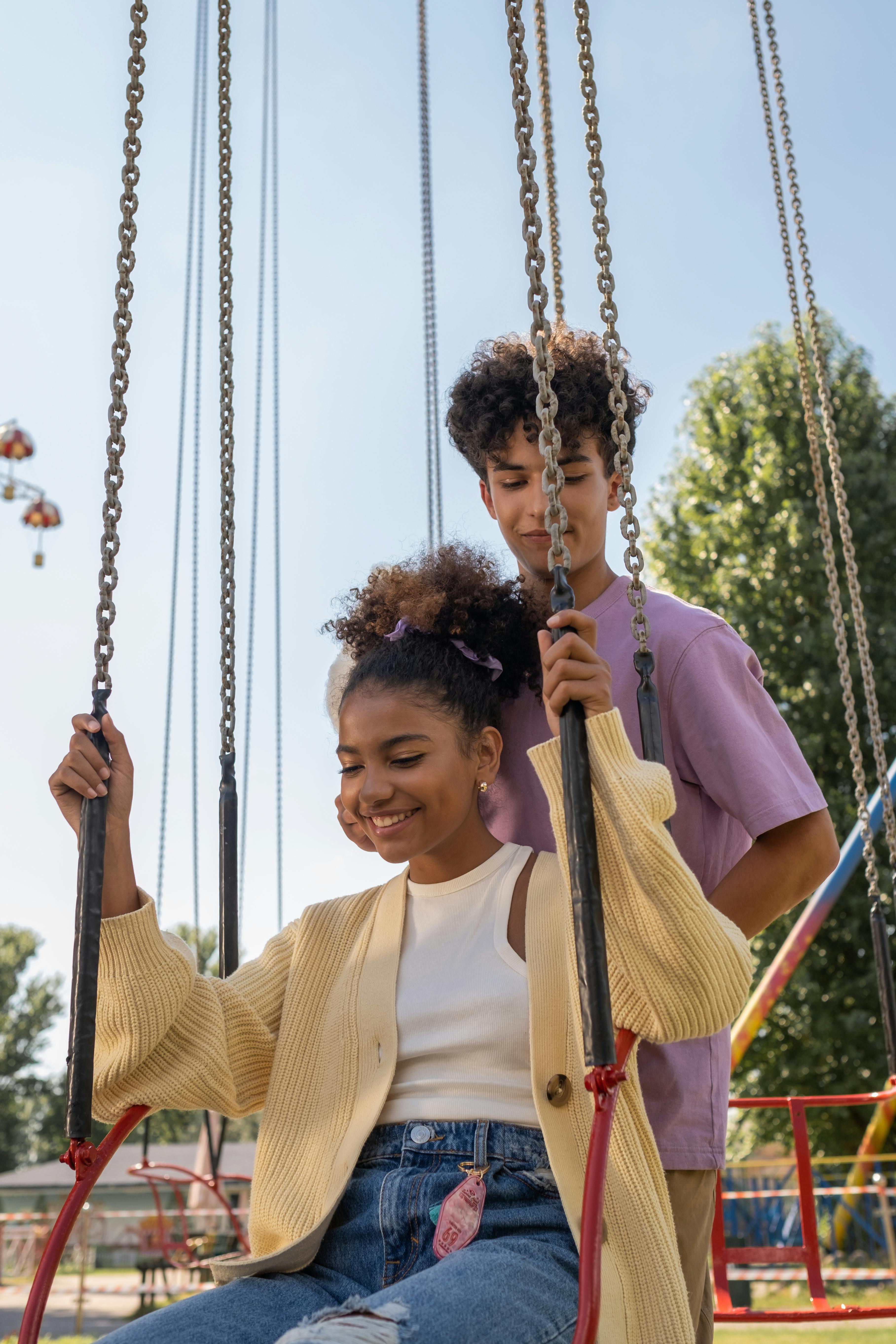 teenage boy standing behind teenage girl sitting in carousel seat