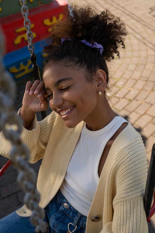 Free Cute black teenage girl sitting in carousel seat with eyes closed and smiling Stock Photo