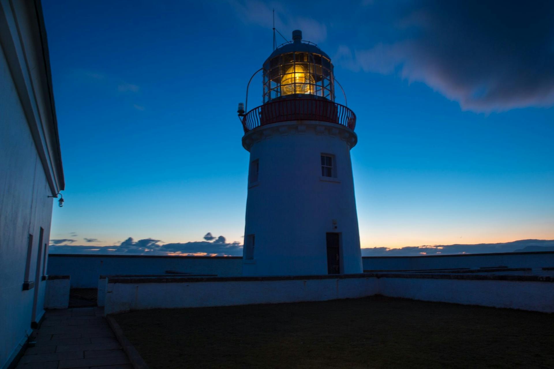 A lighthouse glows against a twilight sky, offering navigational safety.