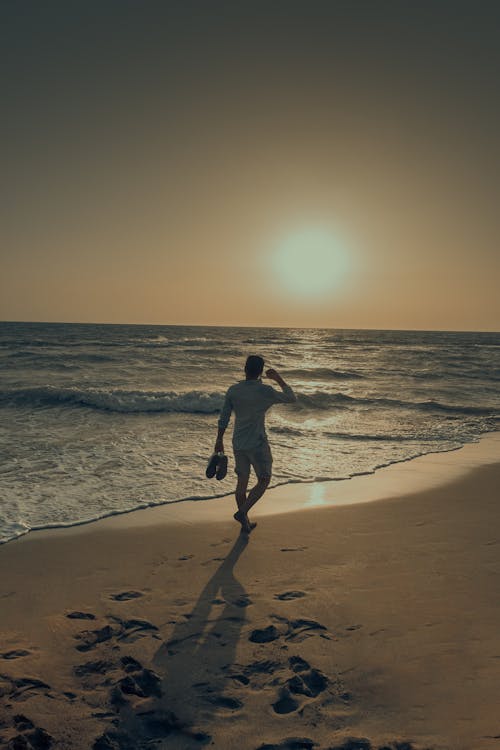 A Person Walking on the Beach during Sunset