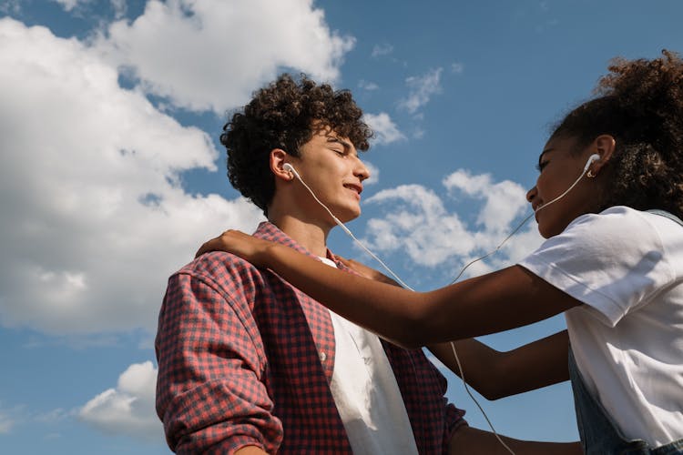 Teenage Couple Sharing Headphones Against Blue Sky