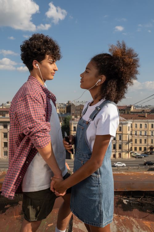 Free Young couple holding hands on a city rooftop, listening to music together, feeling love and connection. Stock Photo