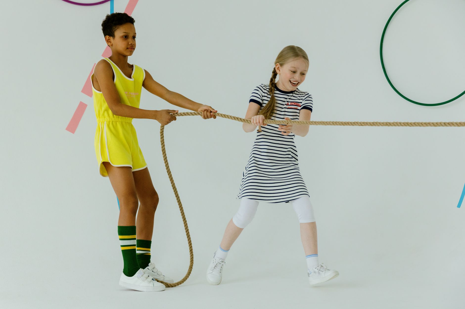 Two children engaging in a playful tug of war game on a white background, showcasing joy and friendship.