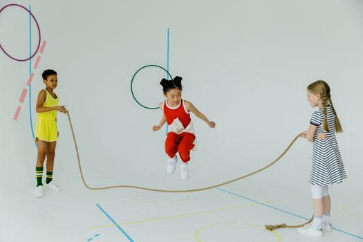 Three diverse children having fun jumping rope in an indoor setting.