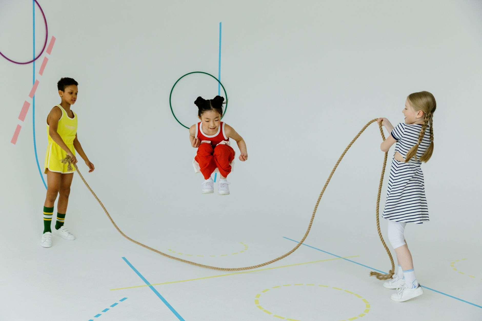 Three children enjoying jump rope play indoors, showcasing fun and diversity.