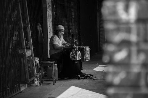 Free Black and white photo of a bearded man sewing on a street, captured in candid style. Stock Photo