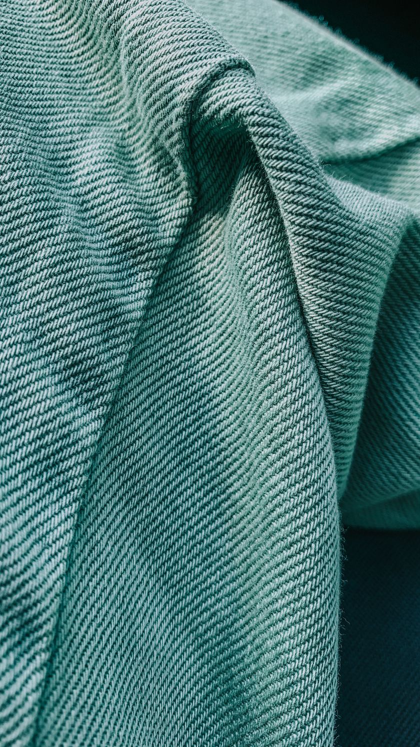 Close-up of a green twill cloth in soft folds, the diagonal twill wale running across the frame