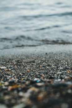 A serene close-up of pebbles on a beach with gentle waves in the background.