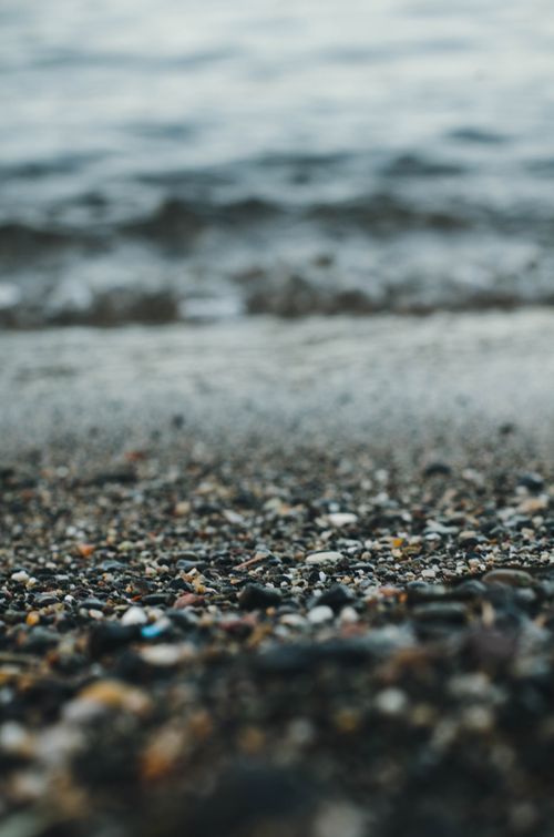 Free A serene coastal scene with pebbles on the beach leading to gentle ocean waves. Stock Photo