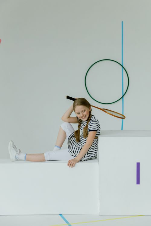 Free Cheerful young girl seated indoors, holding a tennis racket, exuding a sporty vibe. Stock Photo