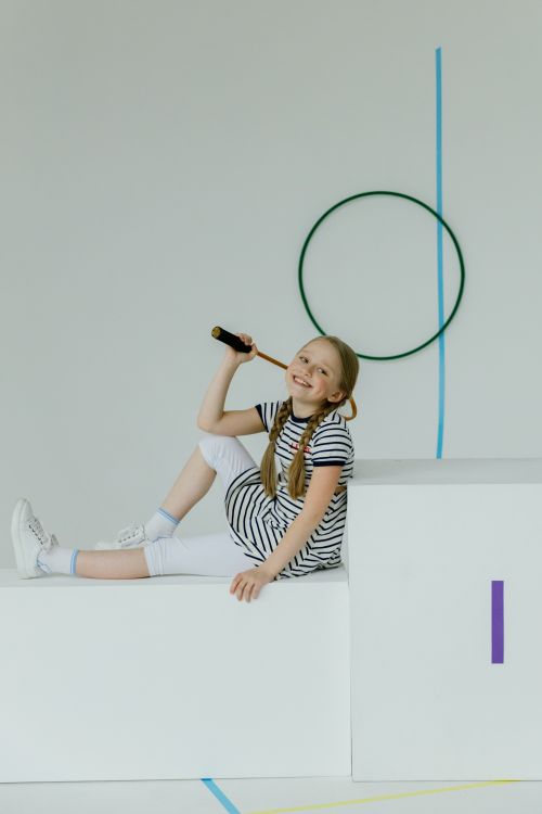 Free Smiling girl in striped dress poses with a jump rope indoors, exuding energetic charm and fun in a minimalist setup. Stock Photo