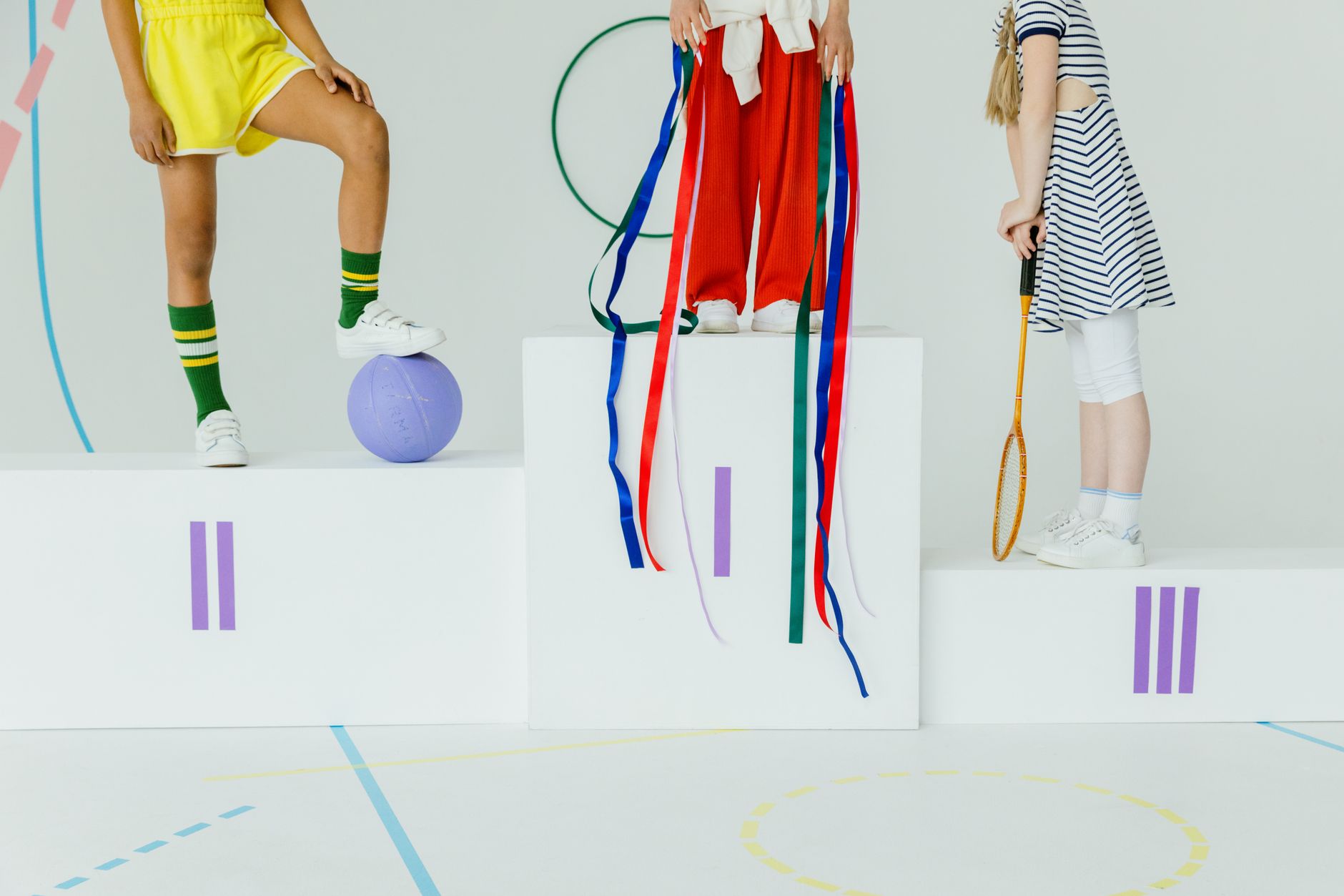Children standing on a podium with sports equipment in a playful setting.