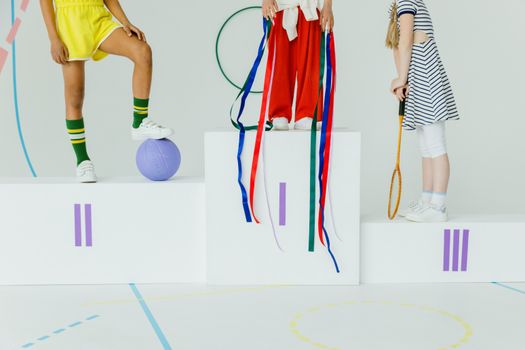 Children standing on a podium with sports equipment in a playful setting.