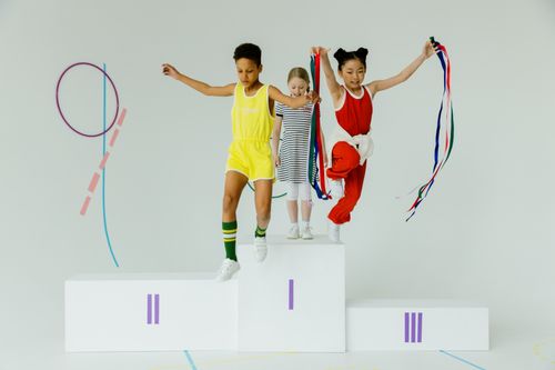 Free Three kids having fun jumping off a podium with colorful ribbons indoors. Stock Photo