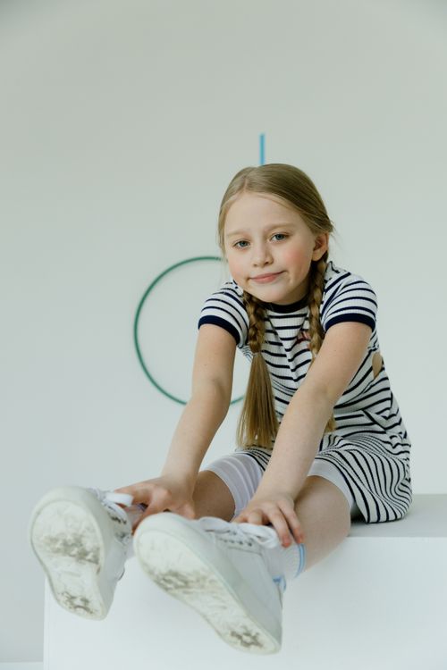 Free Portrait of a smiling girl with braided hair in a striped dress sitting indoors. Stock Photo
