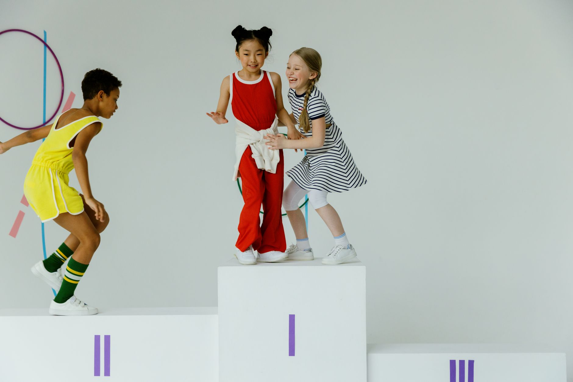 Three children playing joyfully on a sports podium in a bright indoor setting.