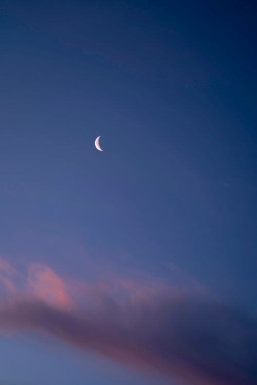 Free A serene view of a crescent moon set against a softly lit evening sky with subtle clouds. Stock Photo
