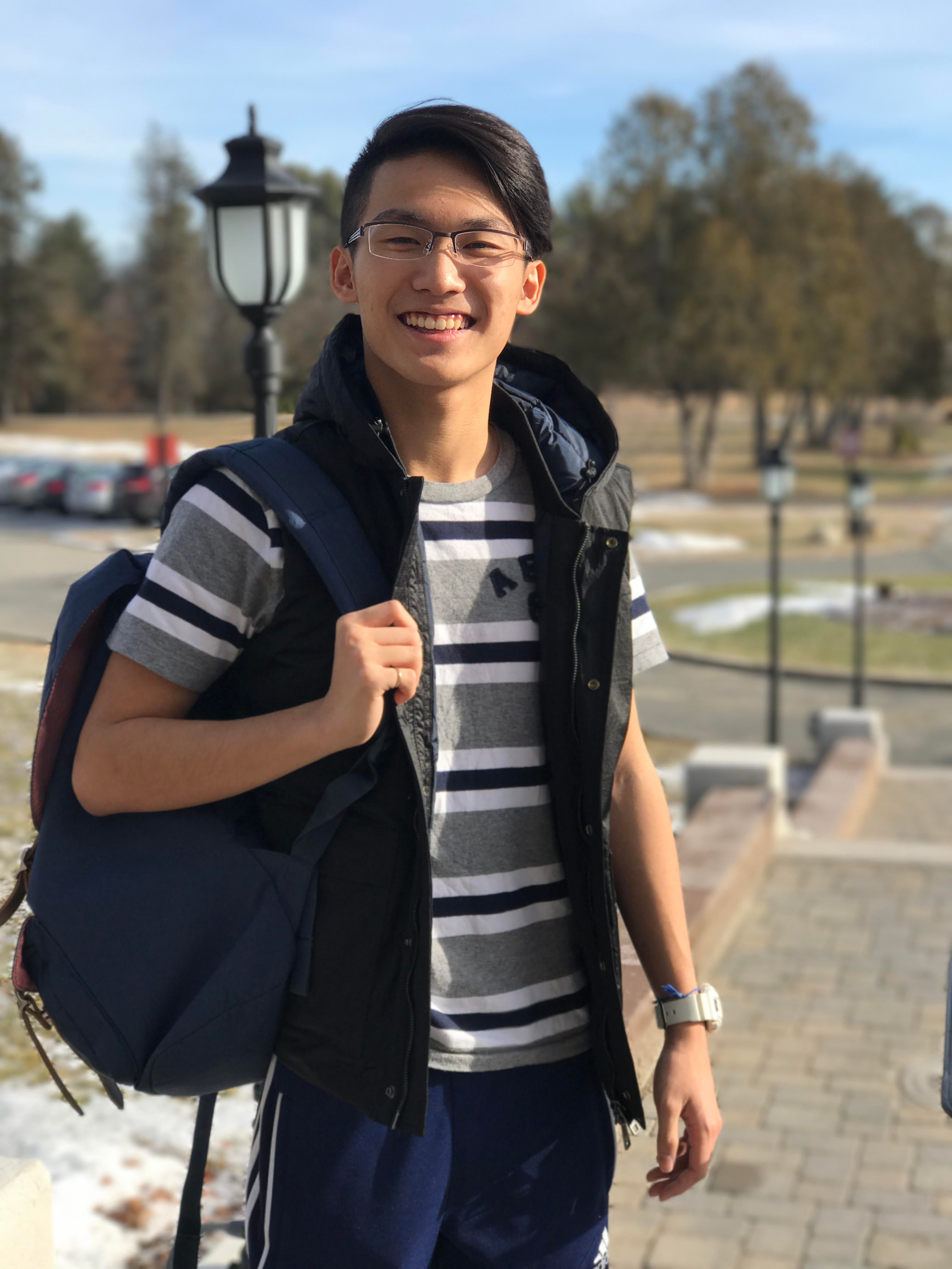 Happy young Asian man smiling outdoors with a backpack on a sunny day.