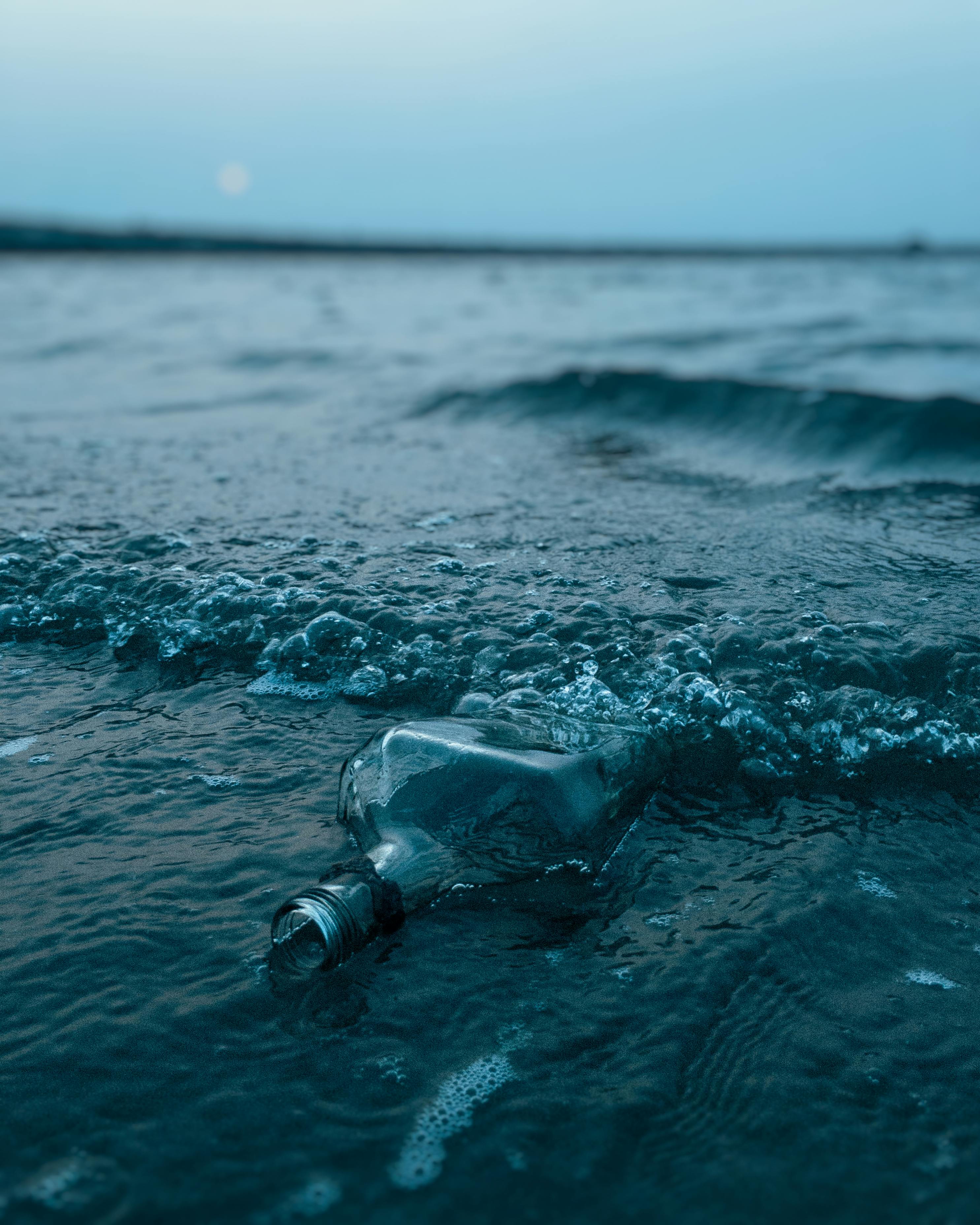 A glass bottle amidst ocean waves, capturing a serene twilight at the beach.