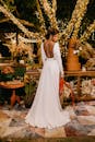 优雅的新娘穿着令人惊叹的白色婚纱，在闪闪发光的树灯下，在户外的花园环境中