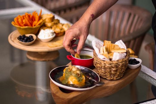 A gourmet platter featuring various breads, cheeses, and a dip with a hand reaching for a piece.