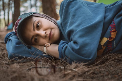 Woman in Blue Hoodie with Headscarf and Cap Lying Down on Brown Grass