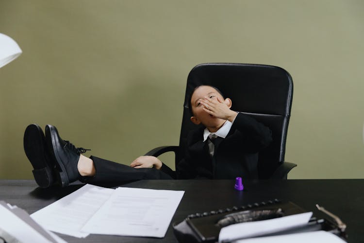 Boy In Black Suit Sitting On Black Office Chair Yawning