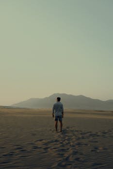 A solitary man on a deserted beach during sunset, evoking feelings of solitude and adventure.