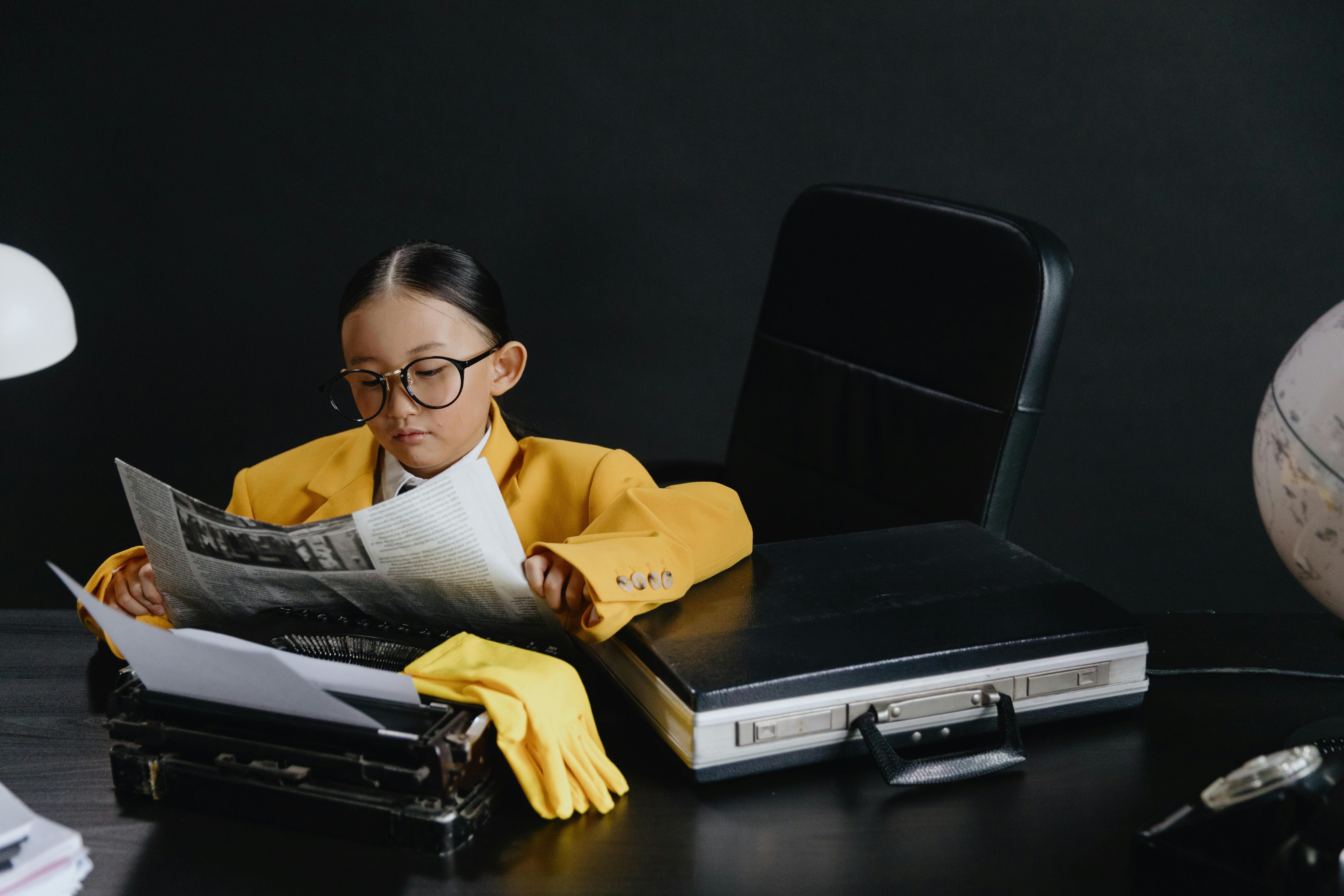 girl in yellow suit sitting by desk and reading newspaper